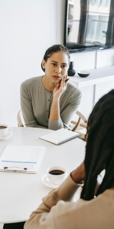 Serious ethnic female consultant listening to black male client problems while sitting at round table together in light psychology center