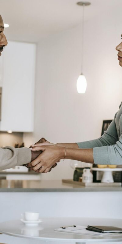 Side view positive multiethnic male client and female psychotherapist in formal clothes shaking hands and looking at each other after psychotherapy session in light modern studio