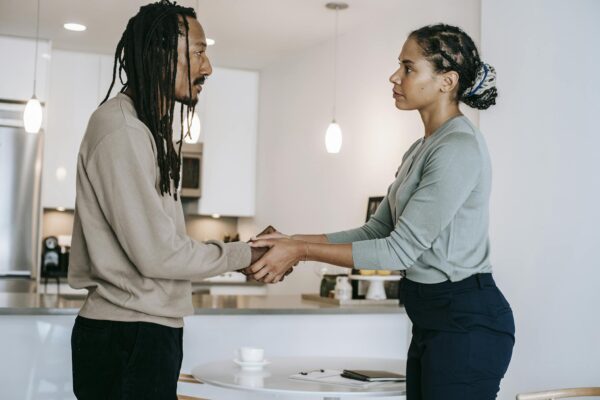 Side view positive multiethnic male client and female psychotherapist in formal clothes shaking hands and looking at each other after psychotherapy session in light modern studio