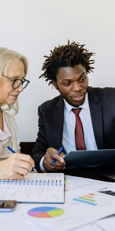 Two business professionals collaborating at a desk with laptops and documents in an office setting.